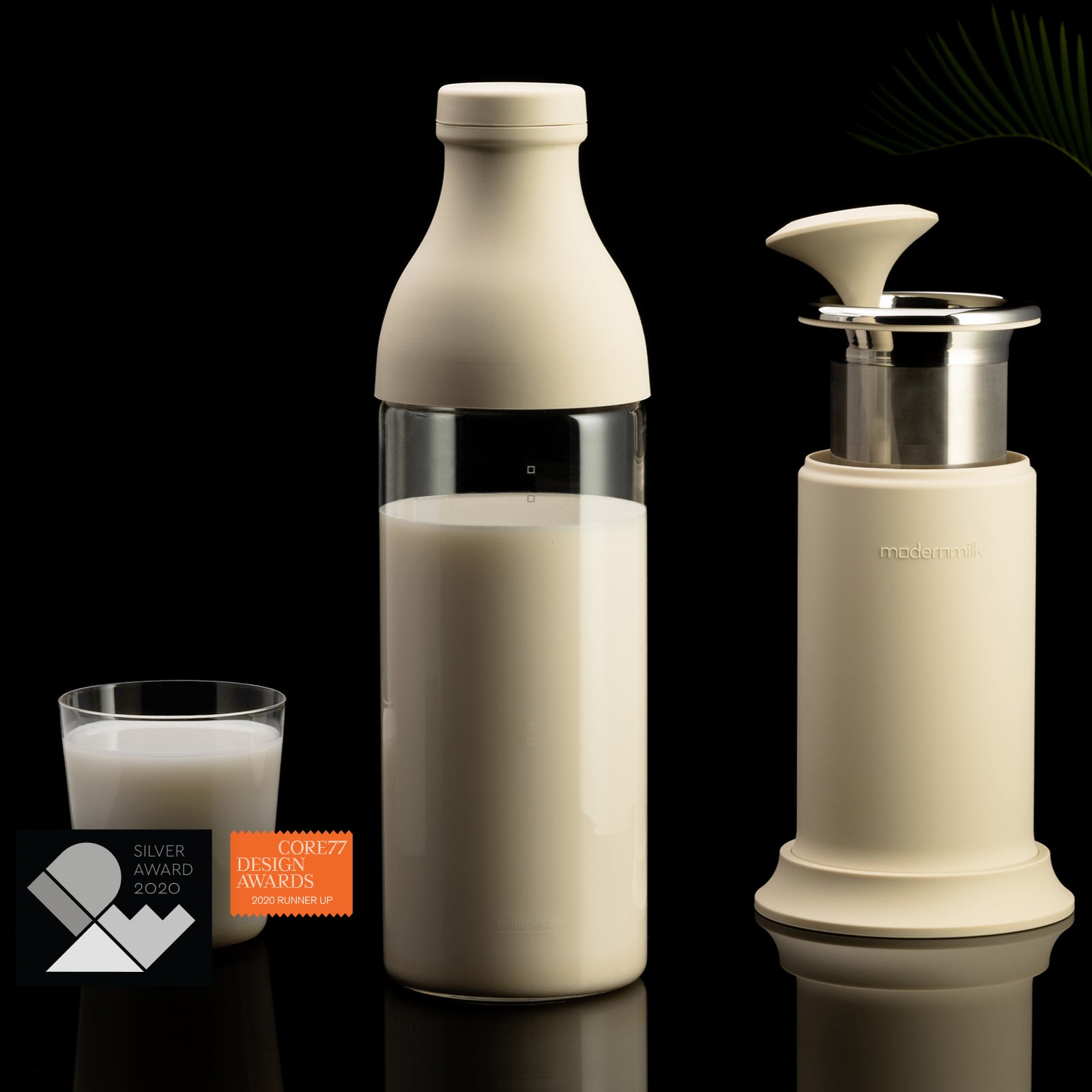 A stylish photo of the cream-colored milkpress bottle full of creamy plant-based milk. It’s next to a glass of plant-based milk as well as the milkpress parts neatly compacted for storage.